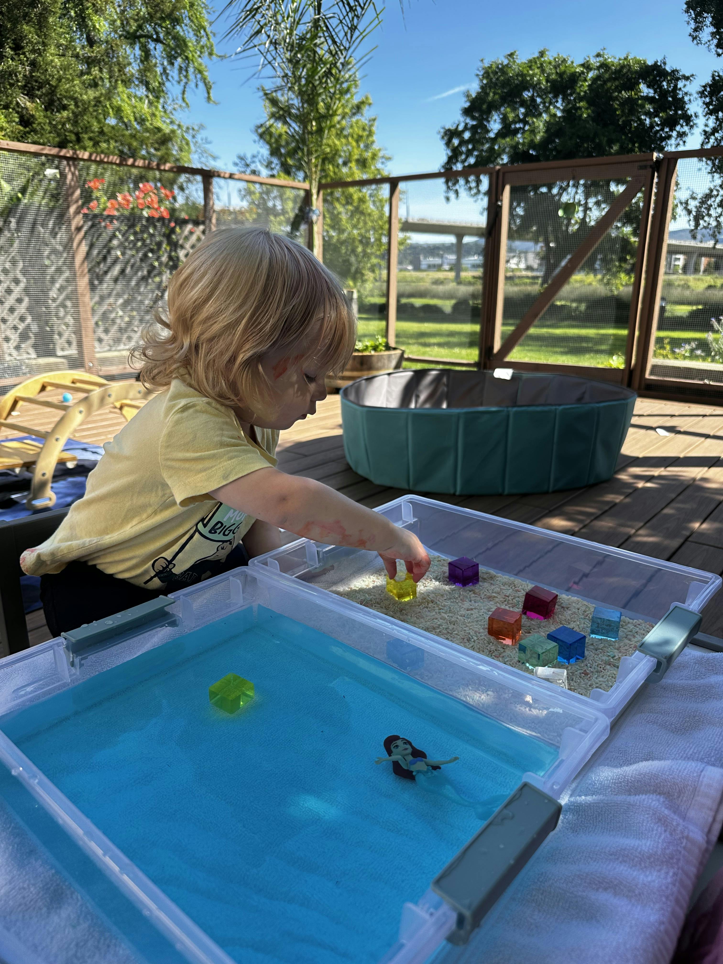 Child playing with toys in water and rice sensory bins on a deck