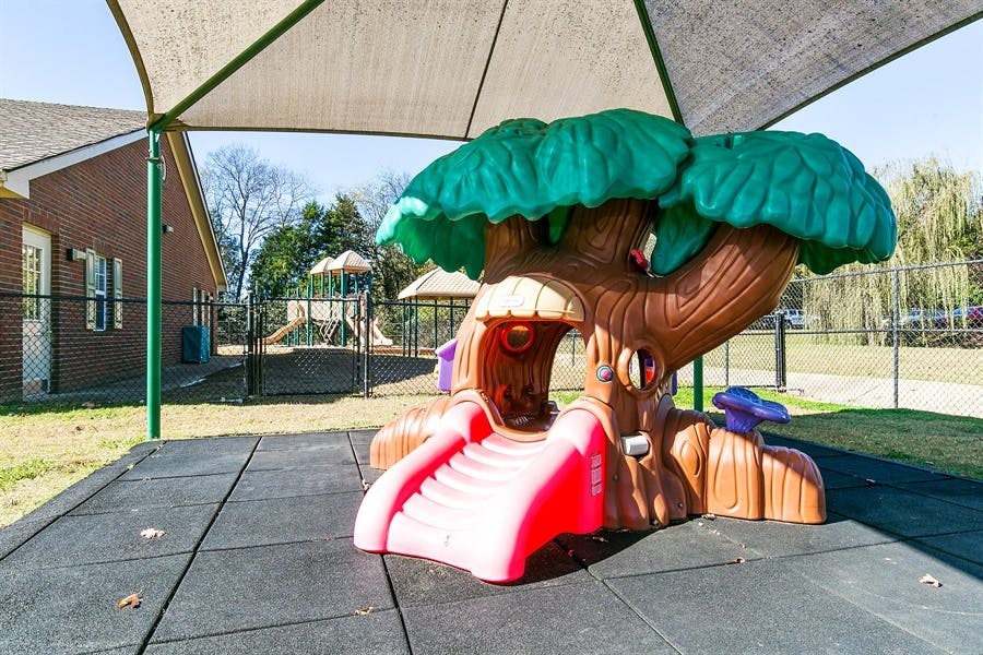 Tree-shaped playground slide on rubber matting under a shade canopy