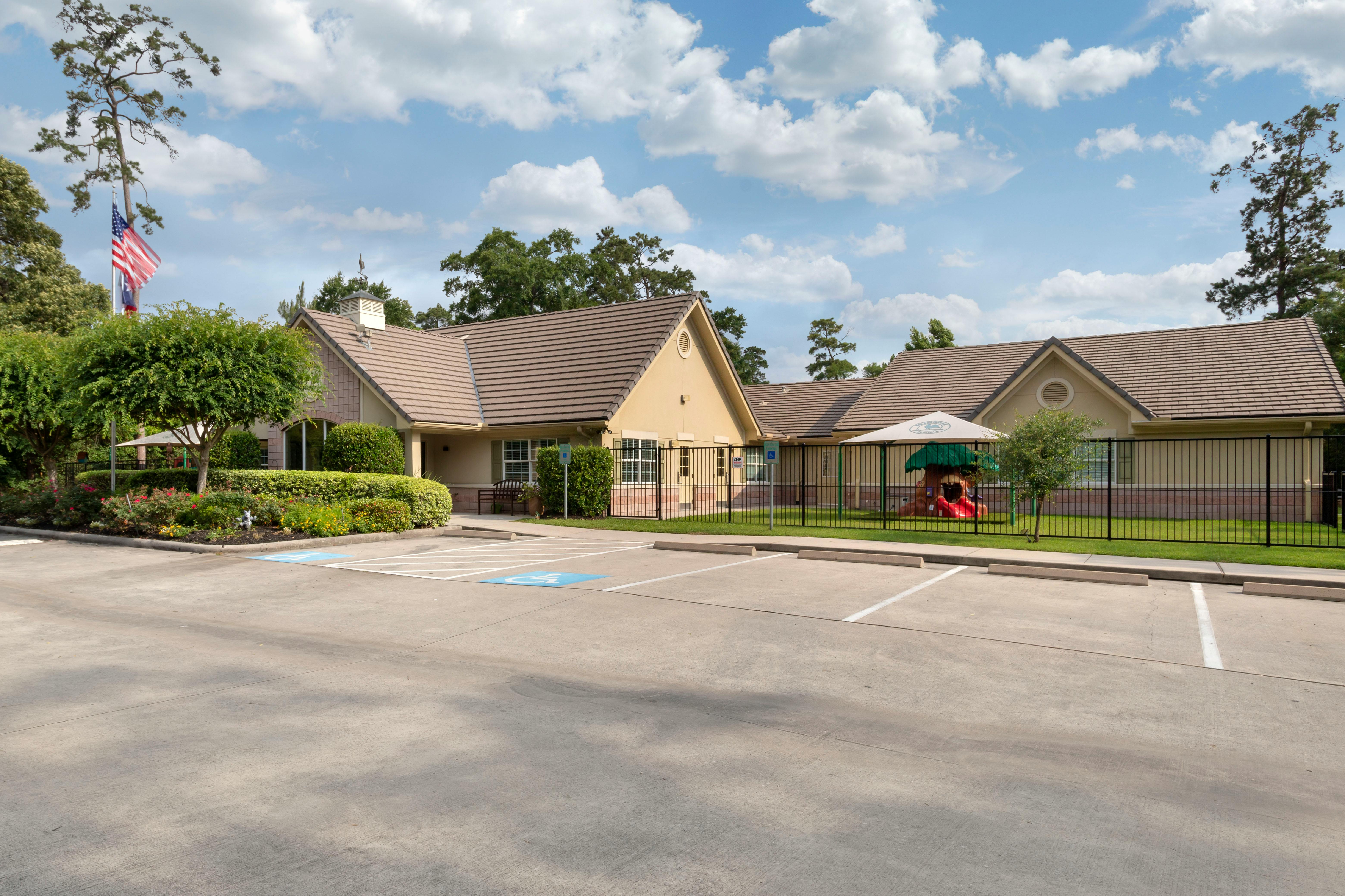 Tan building with brown roof, a fenced playground, and a parking lot