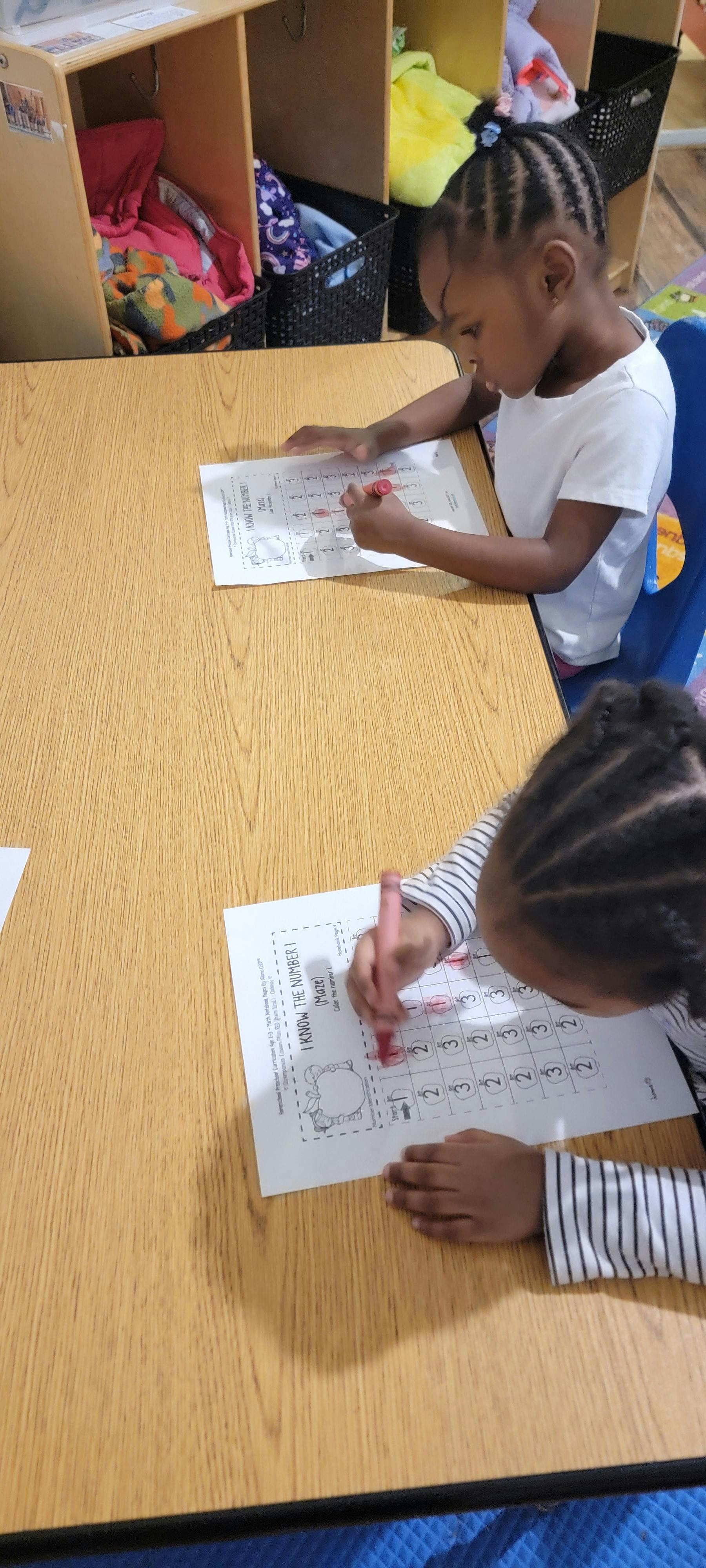 Two children coloring number maze worksheets at a table