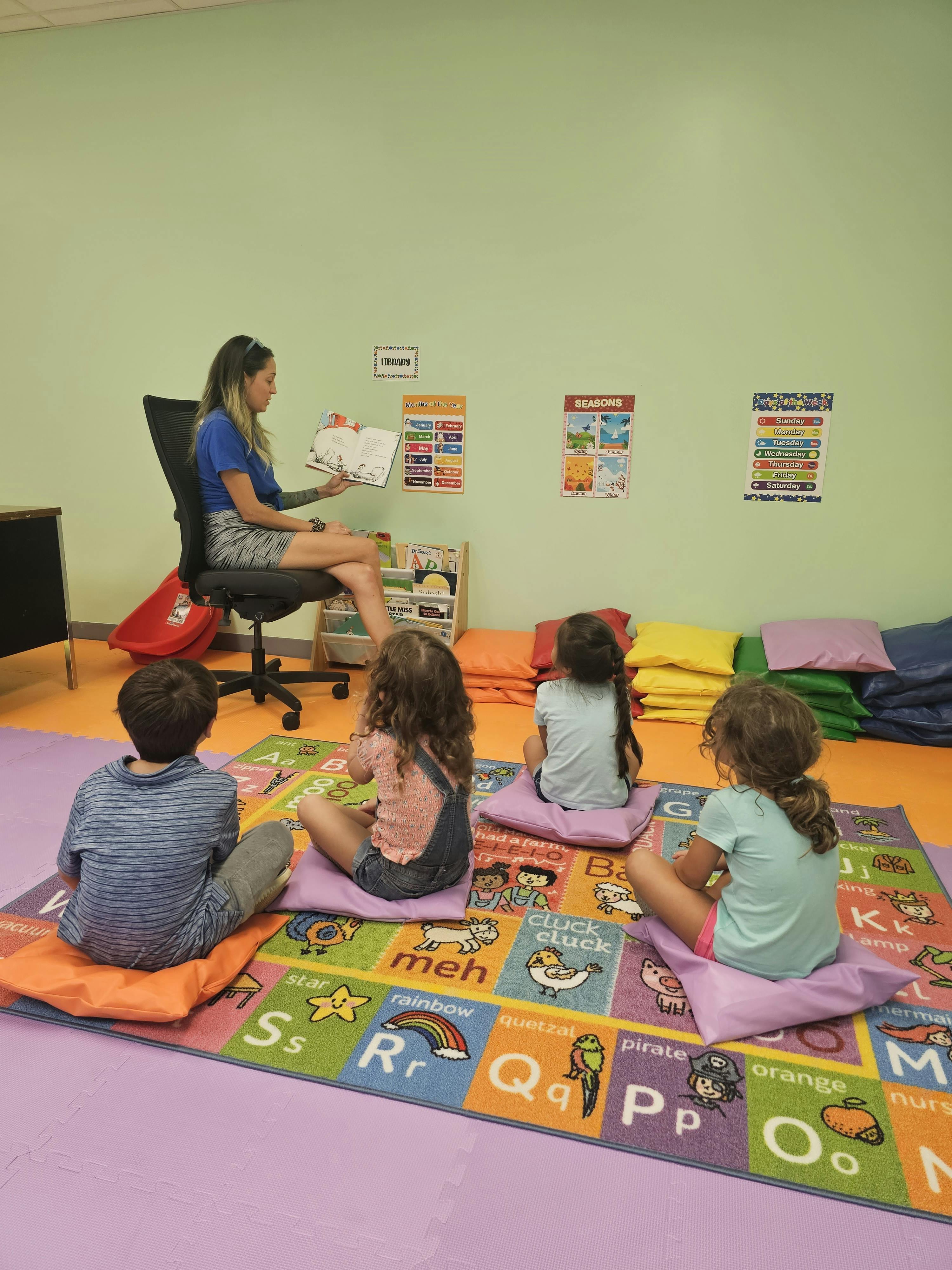 Person reading a book to four children sitting on a colorful alphabet rug
