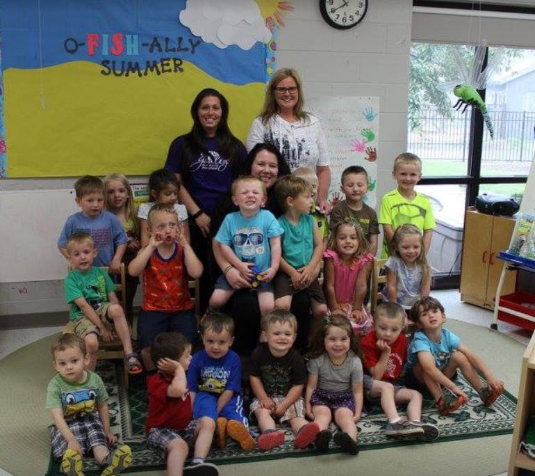 Three adults and many children posing for a group photo in a classroom