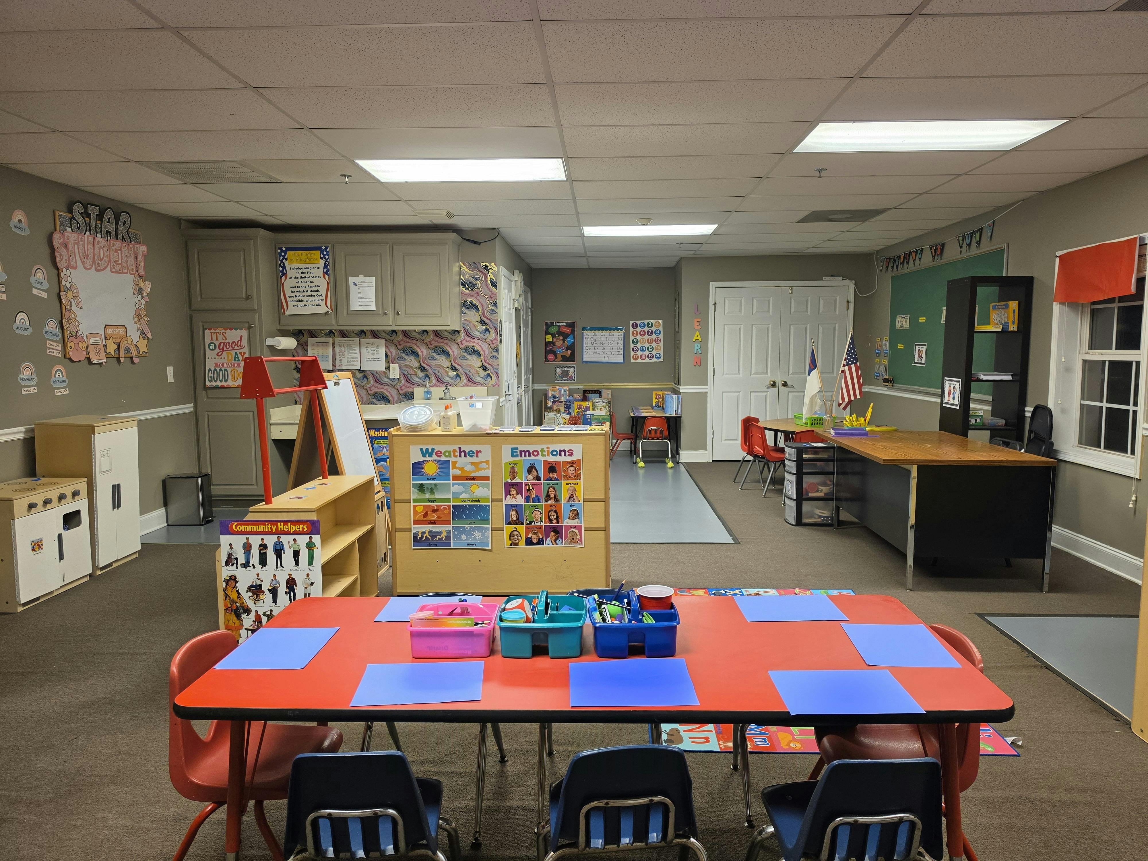 An empty classroom with small tables and chairs arranged, various educational posters