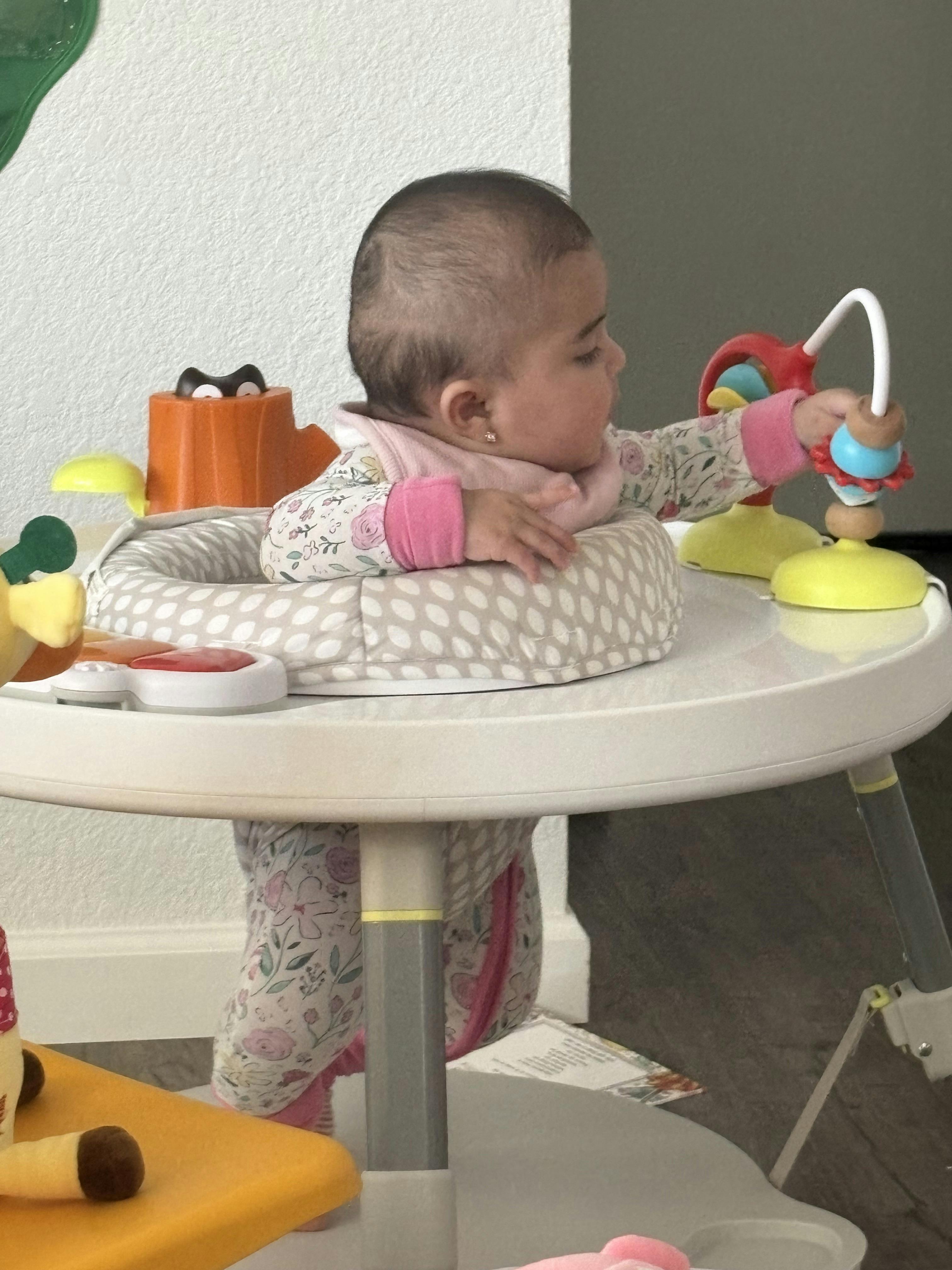 A baby standing in a seated activity center playing with toys