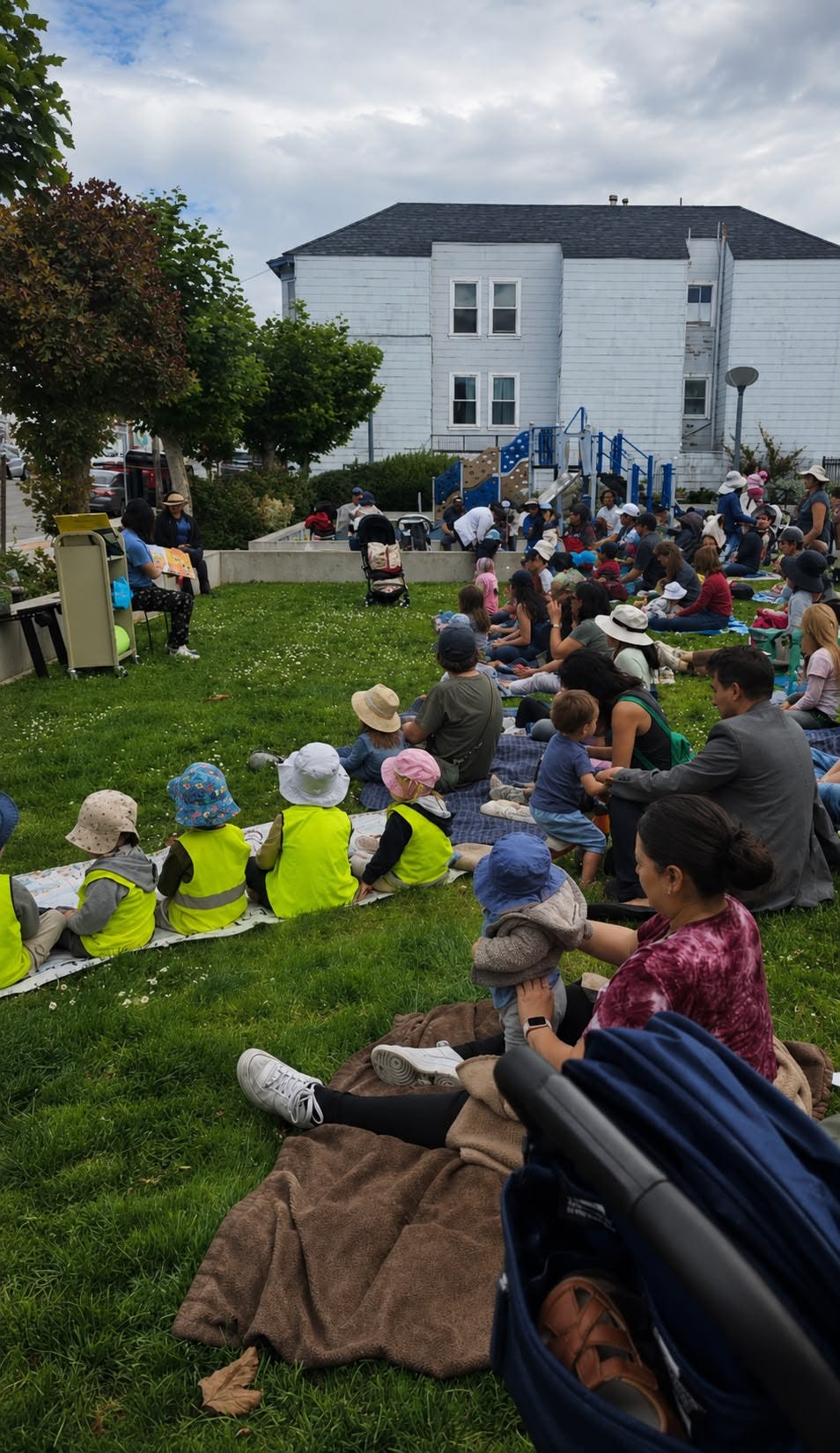 Group of people sitting on grass listening to a person reading a book