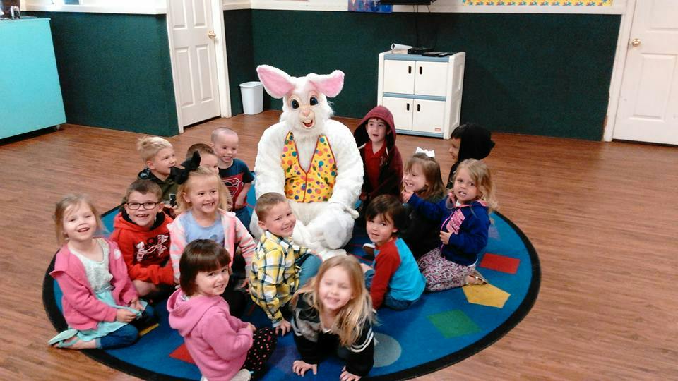 Person in bunny costume sitting with children on a rug