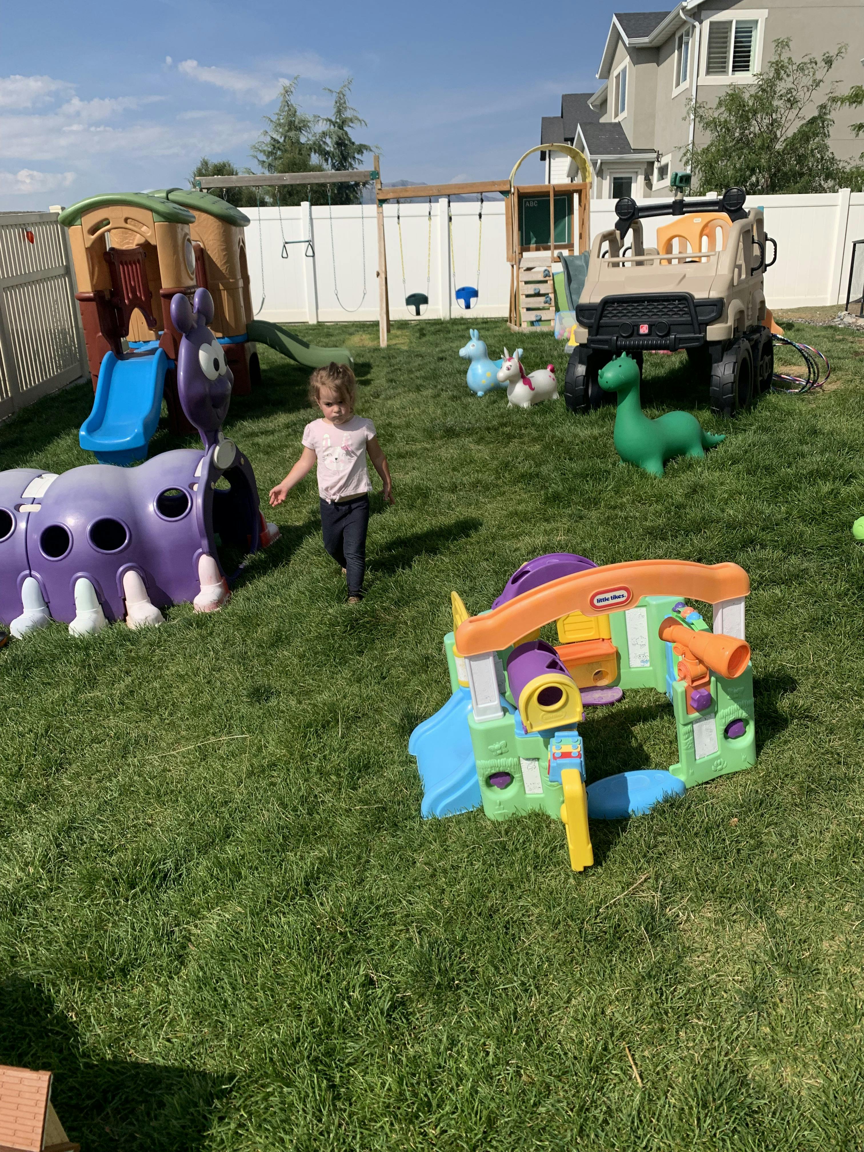 Child walking on grass in a backyard with play structures