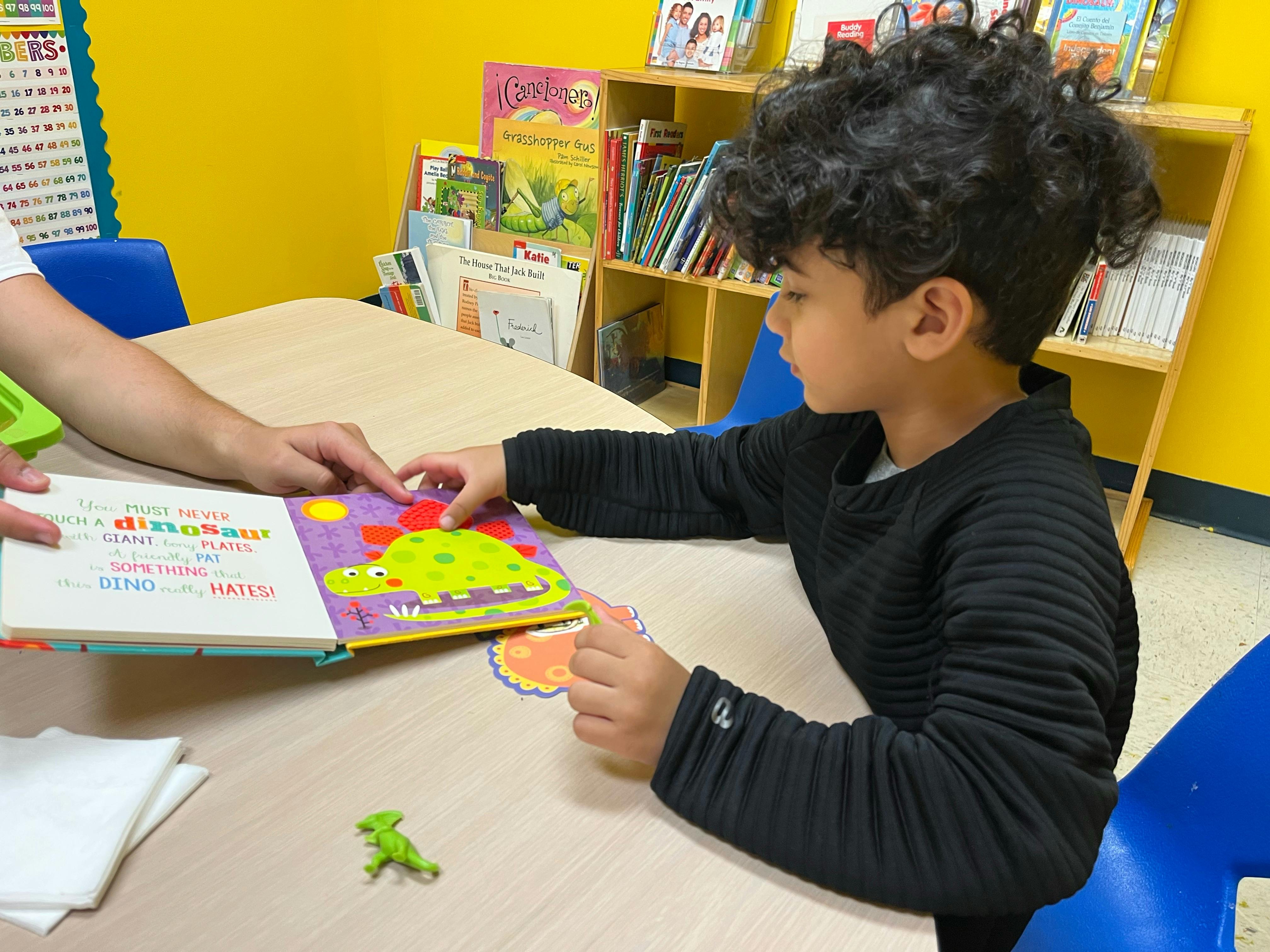 Child and person reading a book together at a table