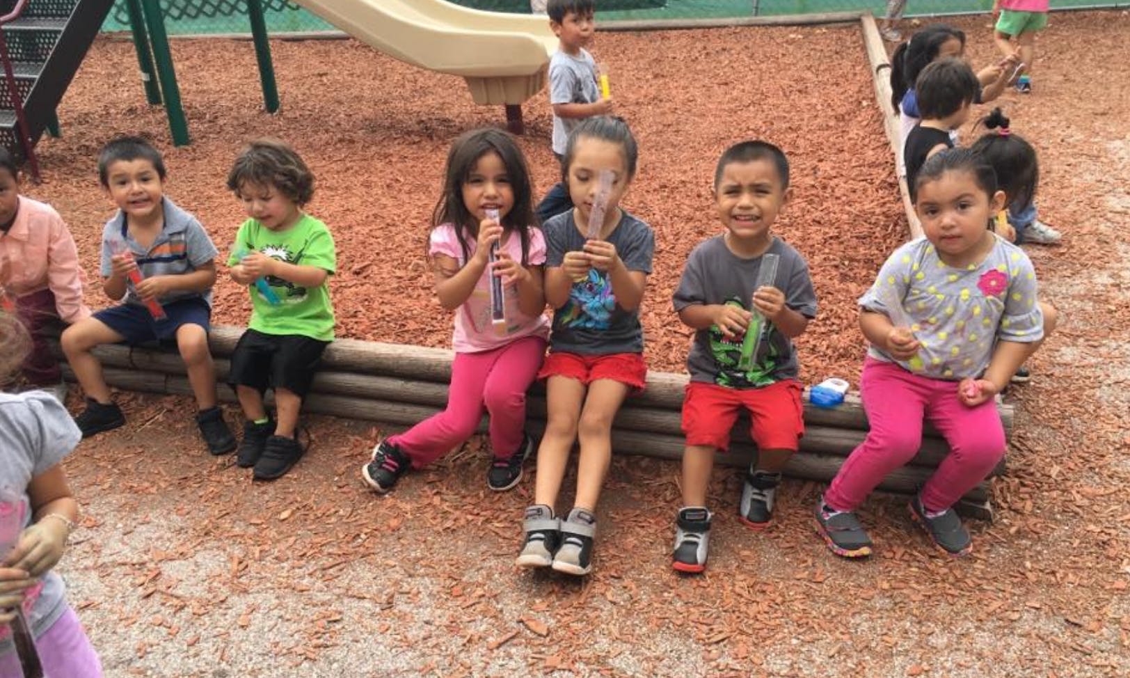 Children sitting on a low wooden barrier on a playground