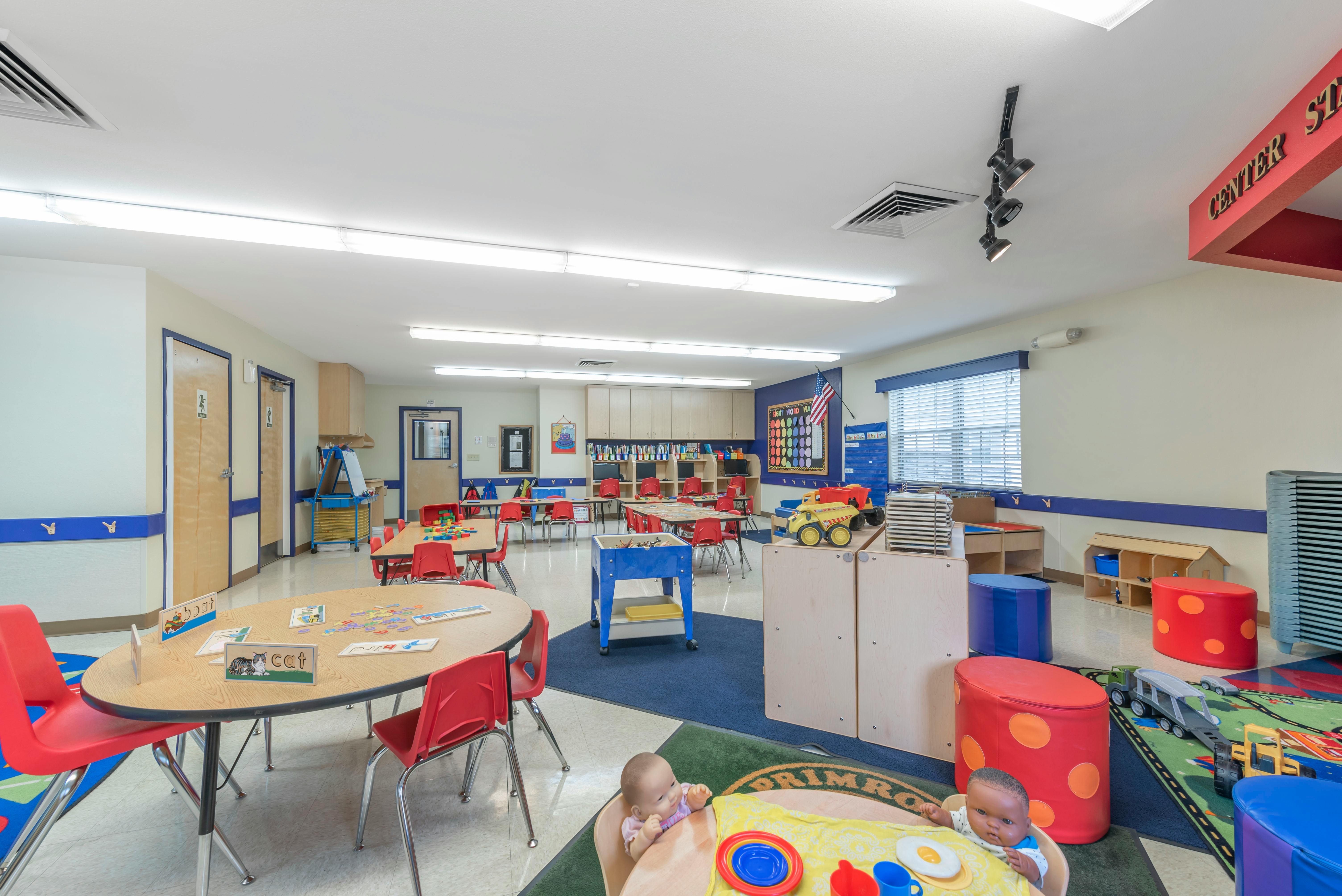 Classroom filled with small tables and chairs, two baby dolls in foreground