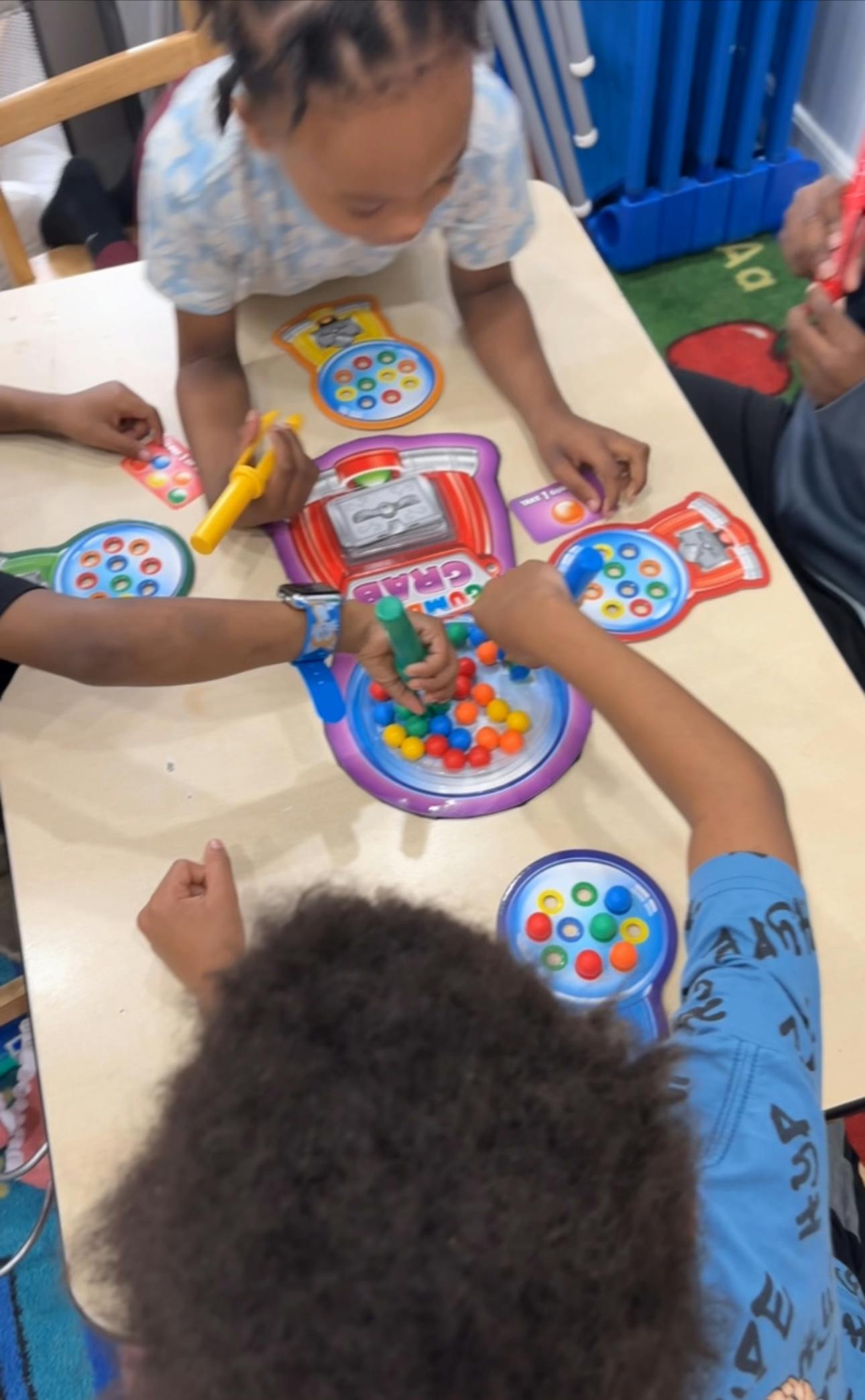 Children playing with colorful beads and toy gumball machines on a table