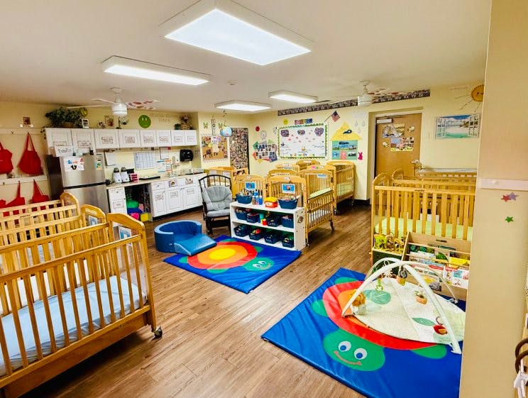 A colorful nursery room with multiple cribs, playmats, and a kitchen area