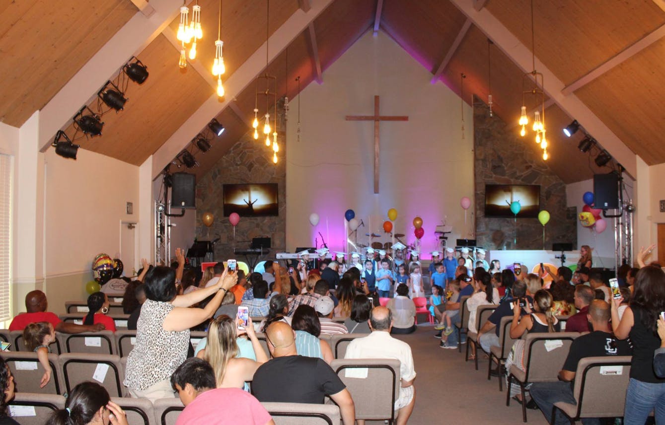 People gathered in a church with a cross on the wall and a stage with balloons