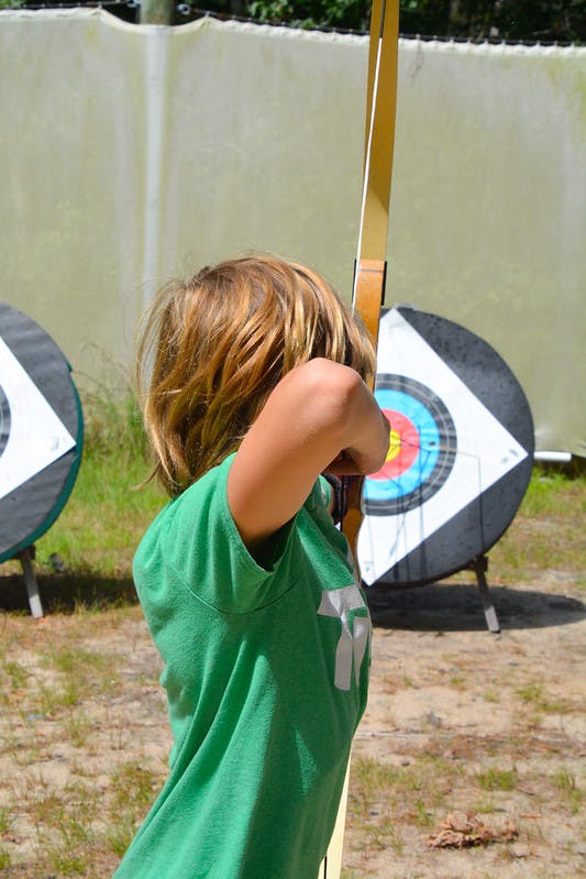 Child aiming a bow and arrow at a target