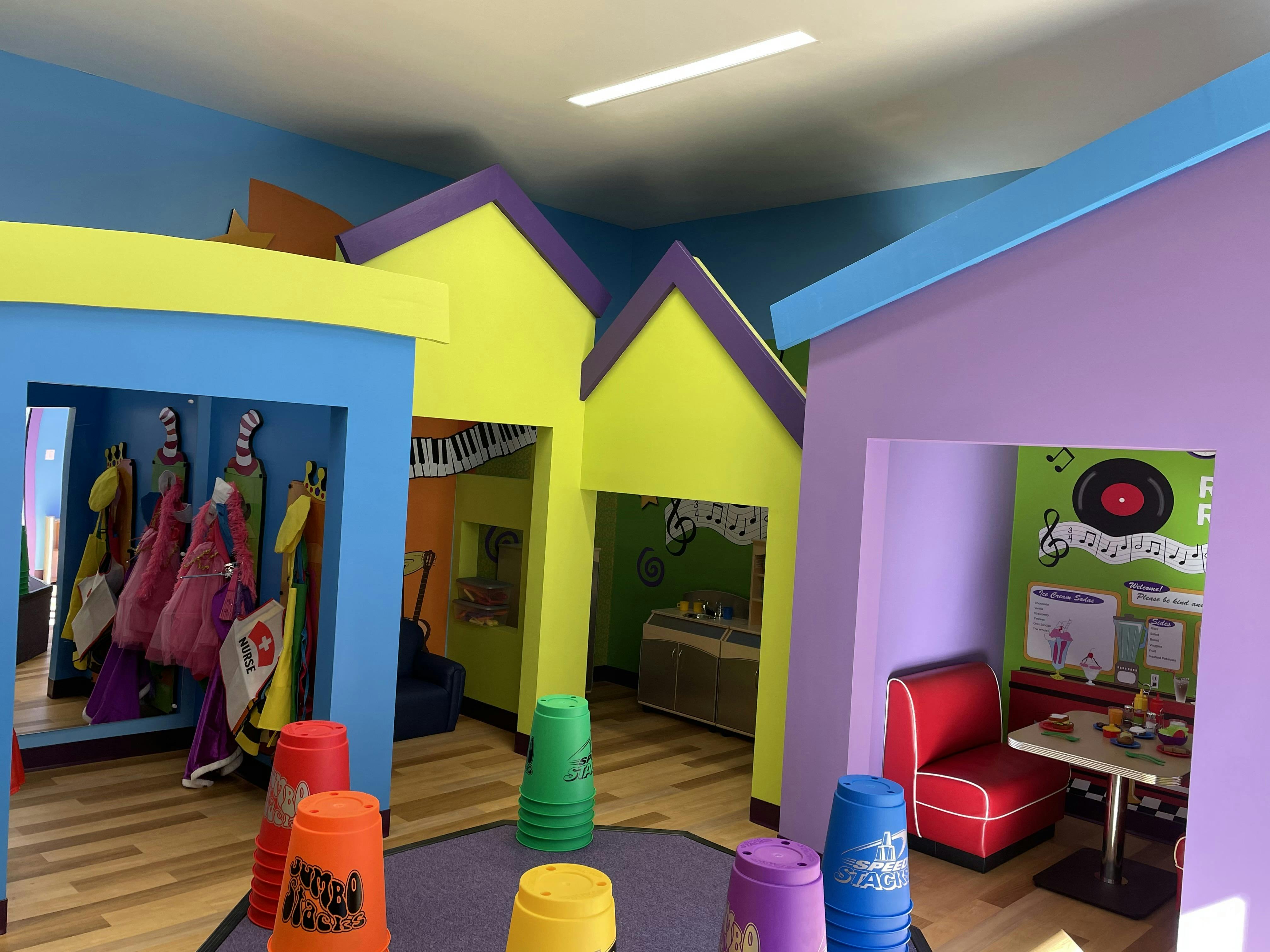 Colorful indoor play area with dress-up clothes, kitchen set, and diner booth