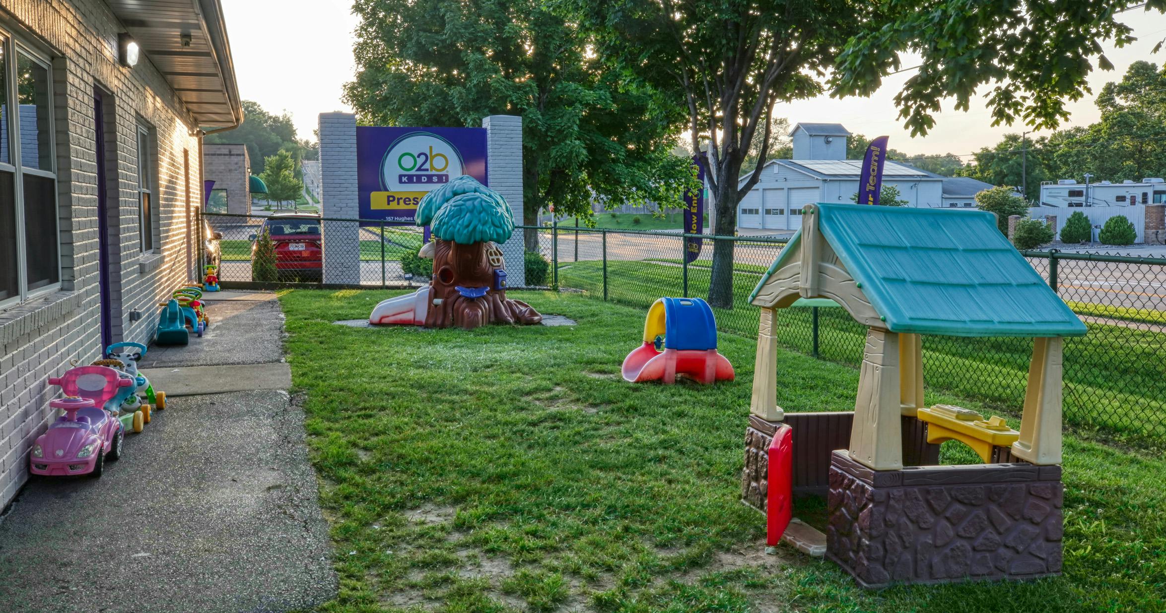 A childcare center playground with a playhouse, tree-shaped slide, and ride-on toys
