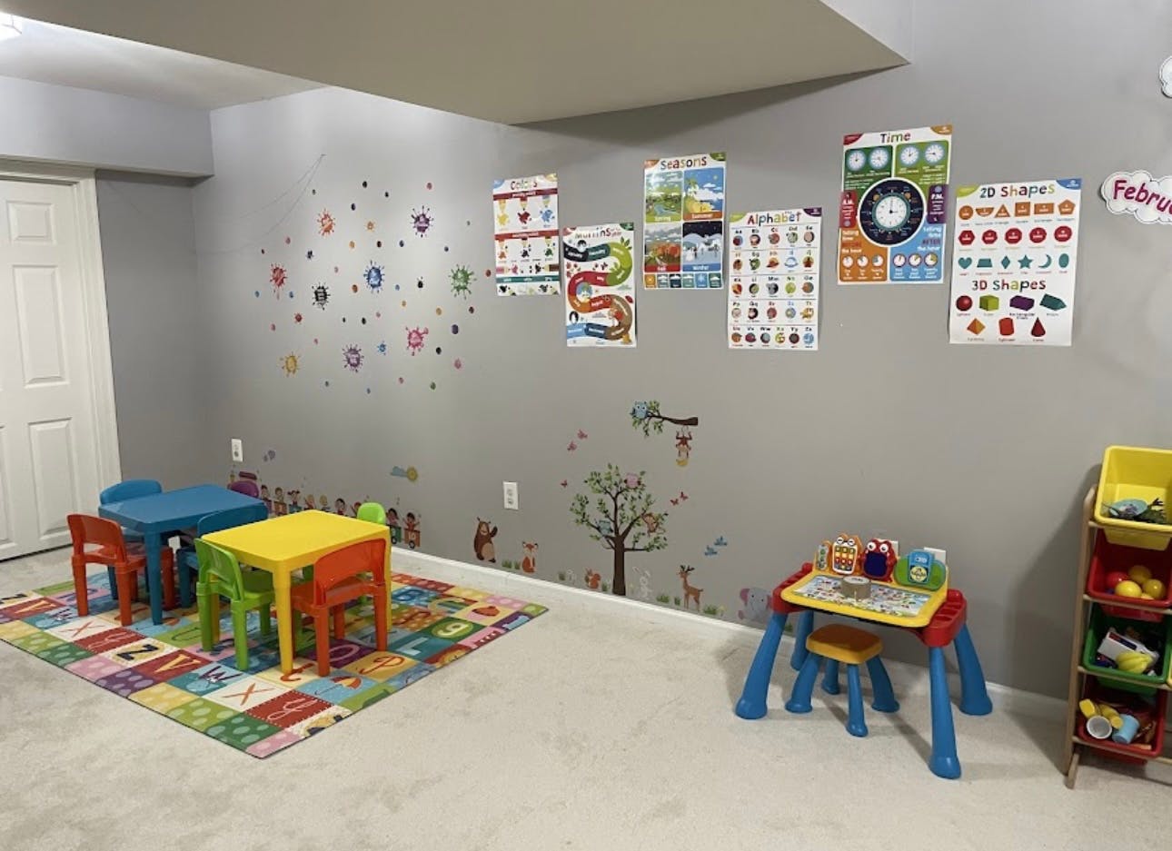 Playroom with small tables and chairs, colorful rug, and educational posters on wall