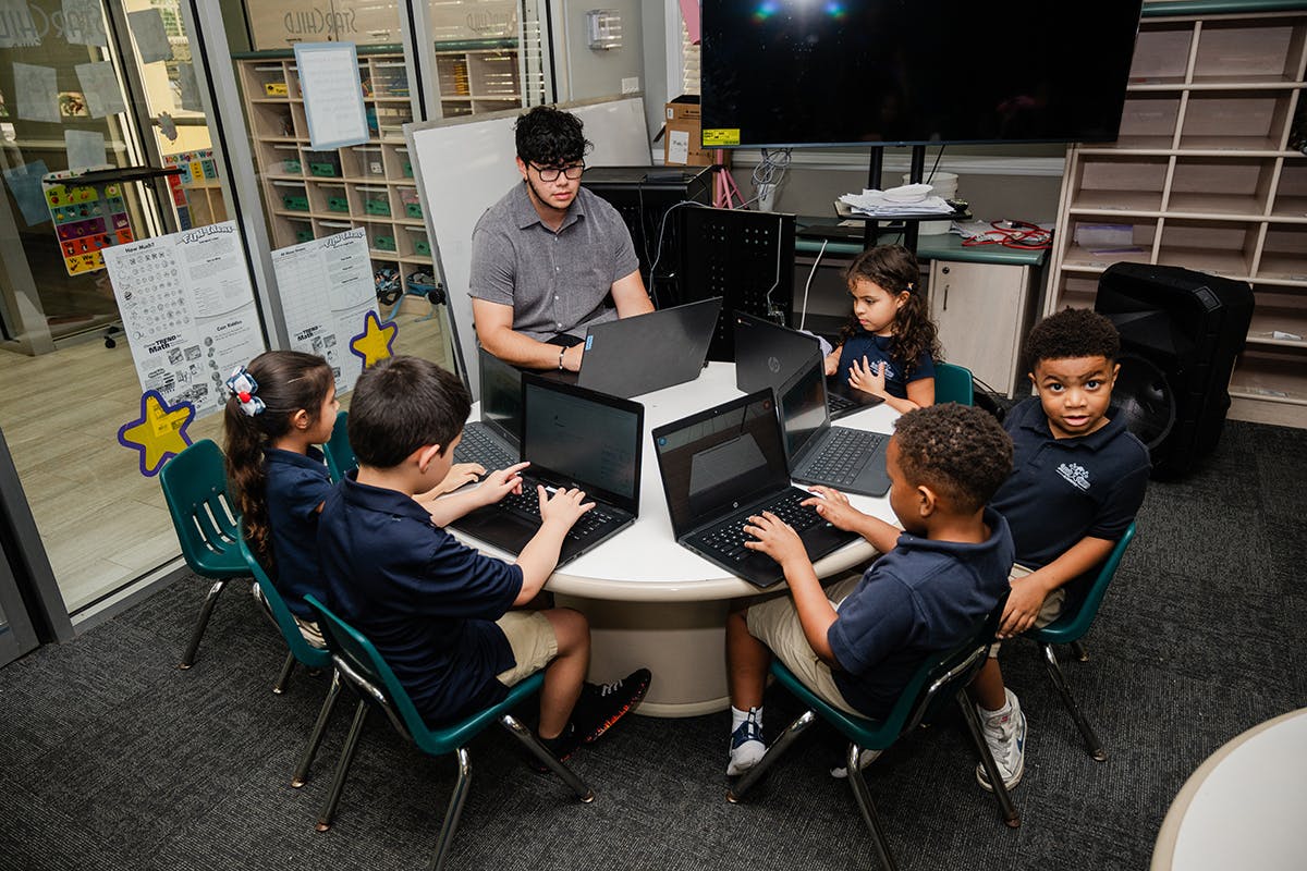 Adult and children working on laptops around a table