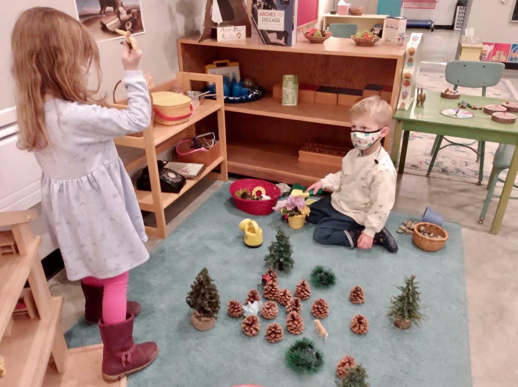 Child in mask playing with pinecones and miniature trees on a rug