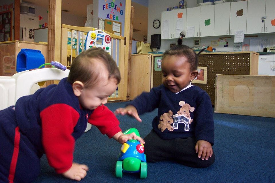 Two children playing with a toy car on the floor in a classroom