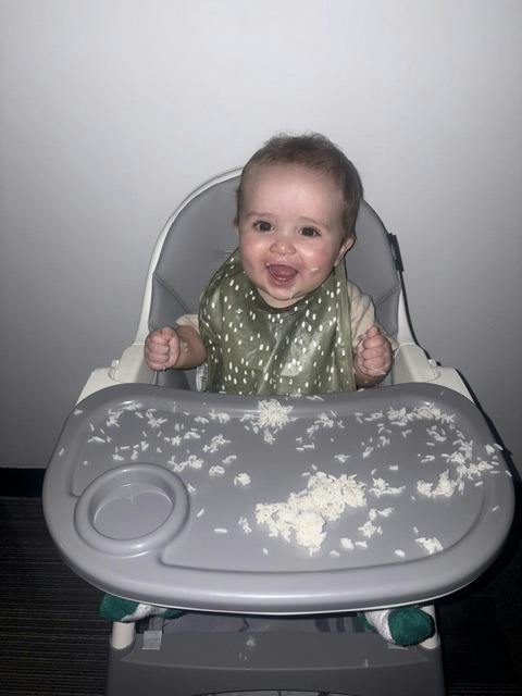 Child sitting in a high chair with scattered rice on the tray