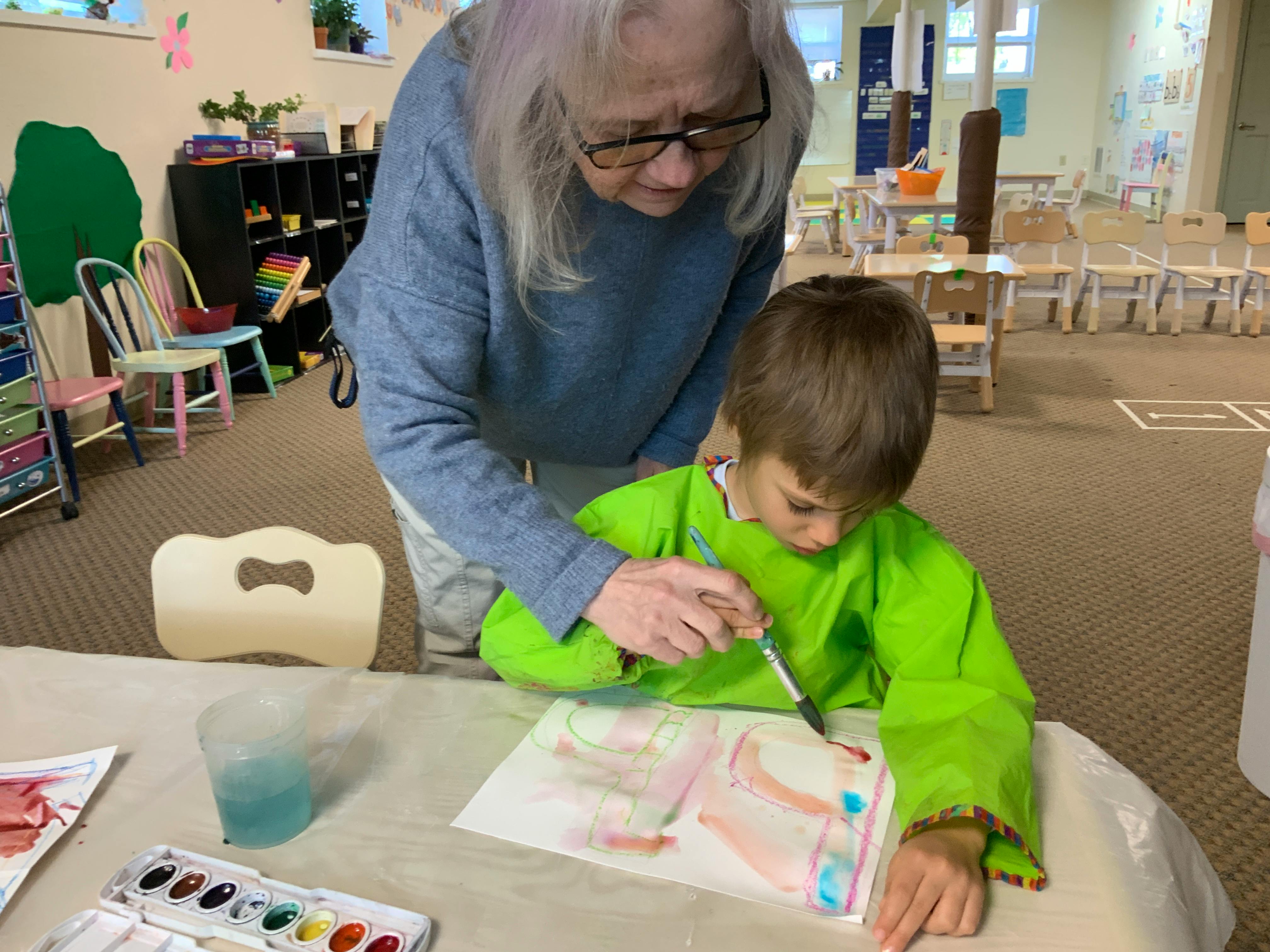 Adult and child painting on paper in a classroom