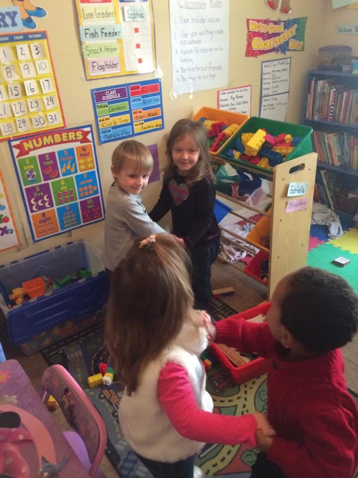 Four children holding hands in a circle in a classroom