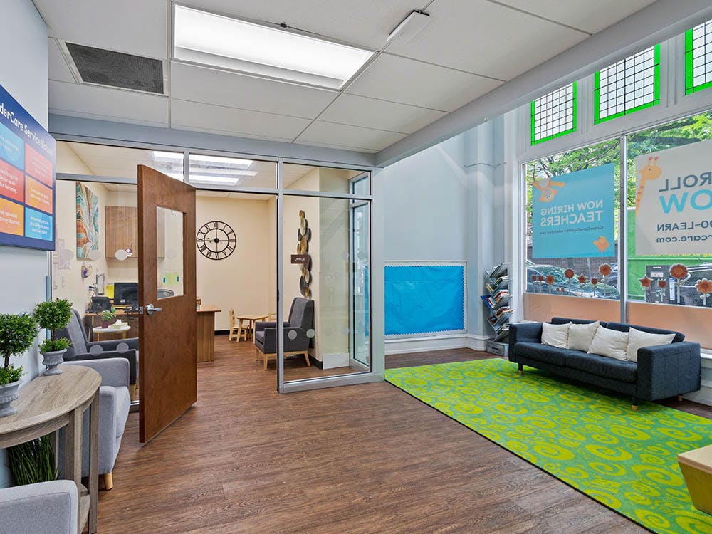 waiting area with a couch, bright green rug, and glass-paneled offices