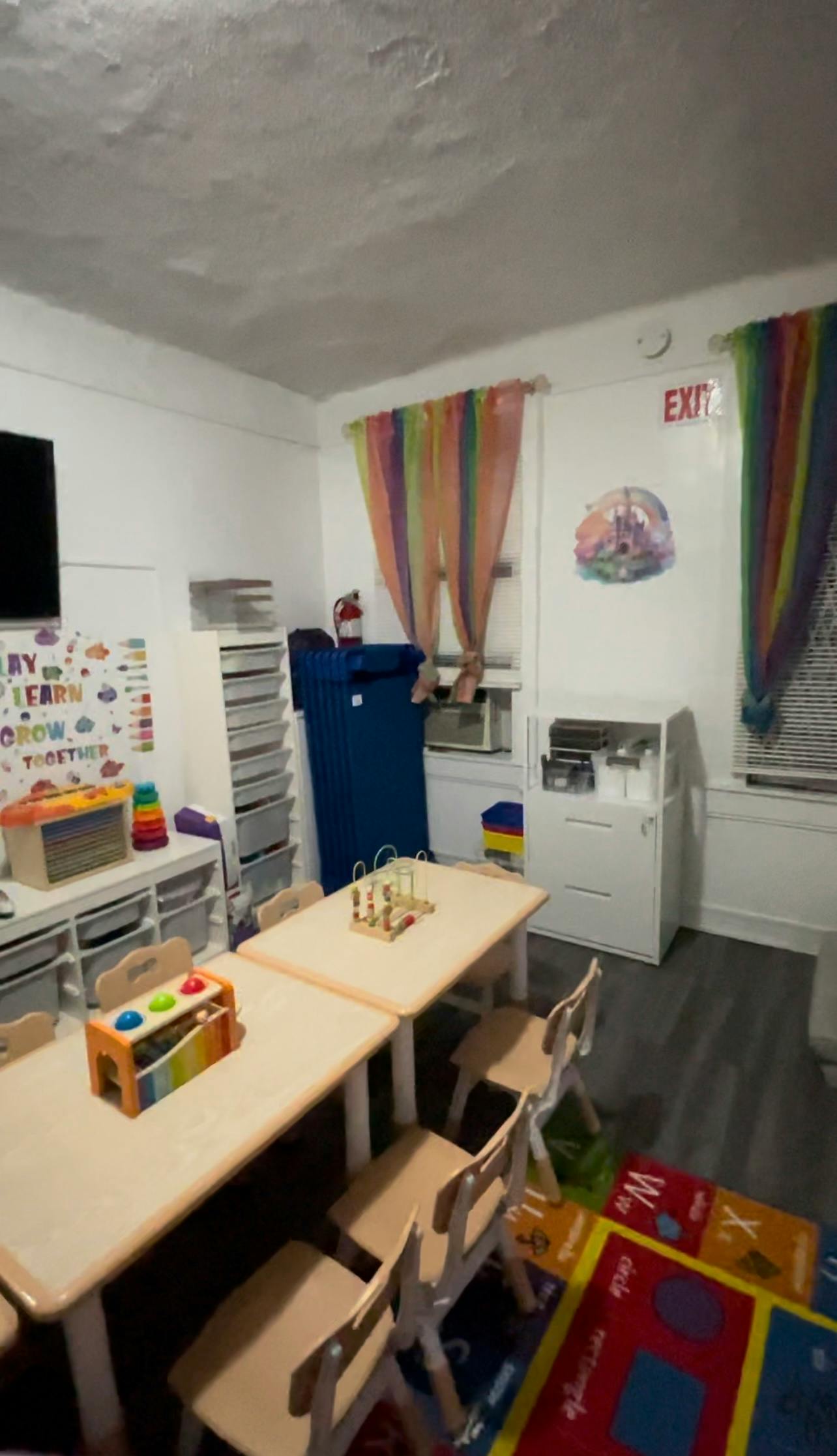 Classroom with small tables and chairs, colorful curtains, and an EXIT sign