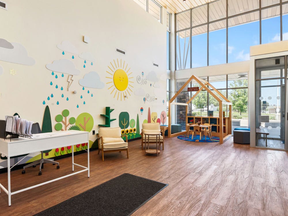 Child-friendly room with wall art depicting sun and clouds, and a wooden playhouse