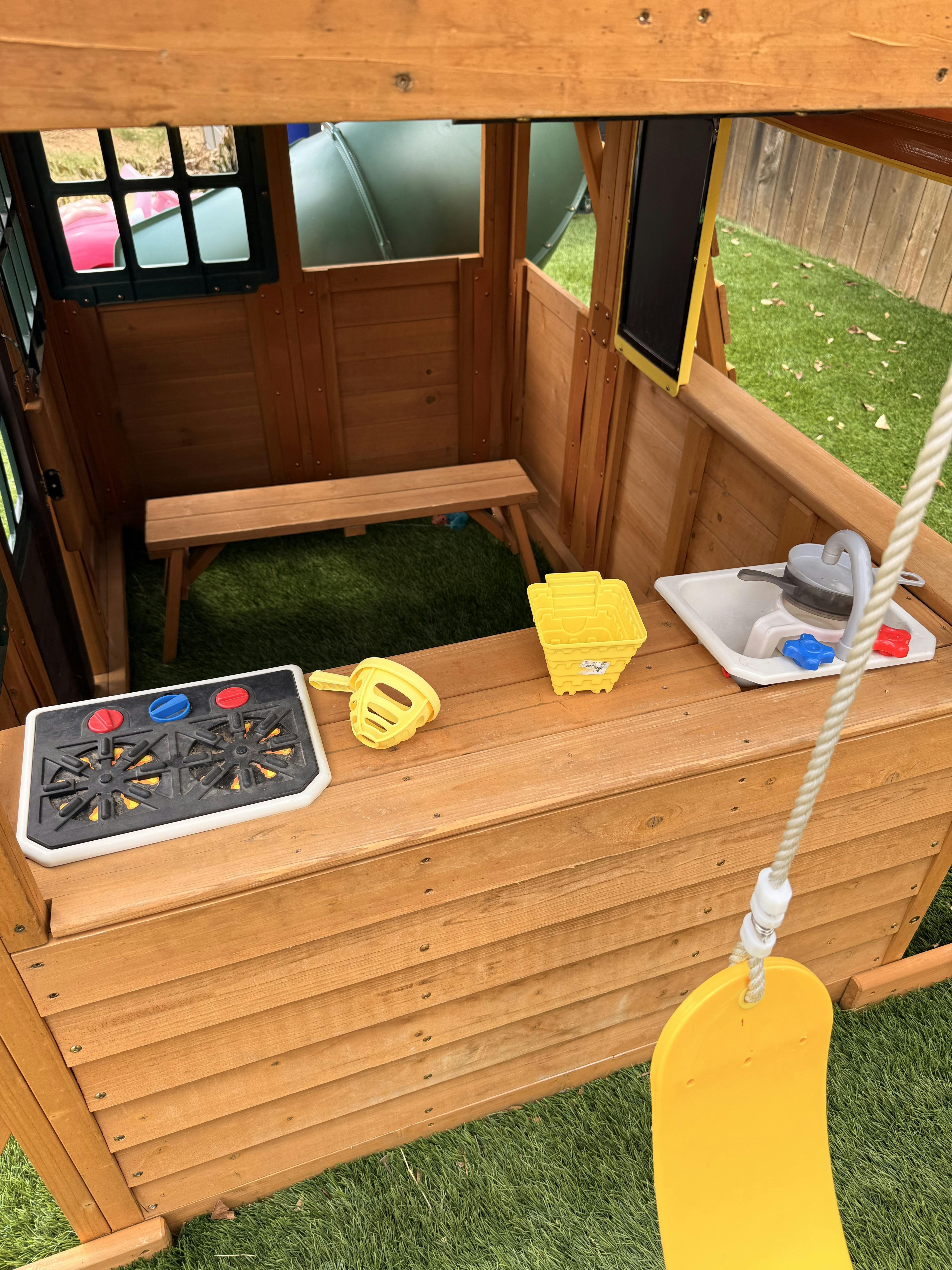 Wooden playhouse with a toy stove, sink, and bench