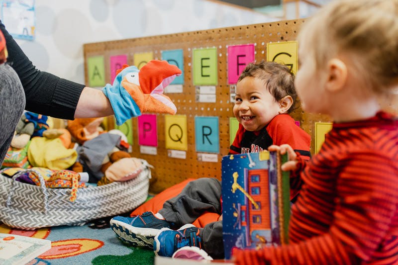 Person using a puppet to interact with two children in a classroom