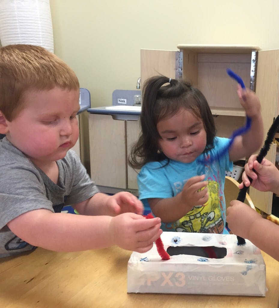 Two children playing with pipe cleaners and a tissue box