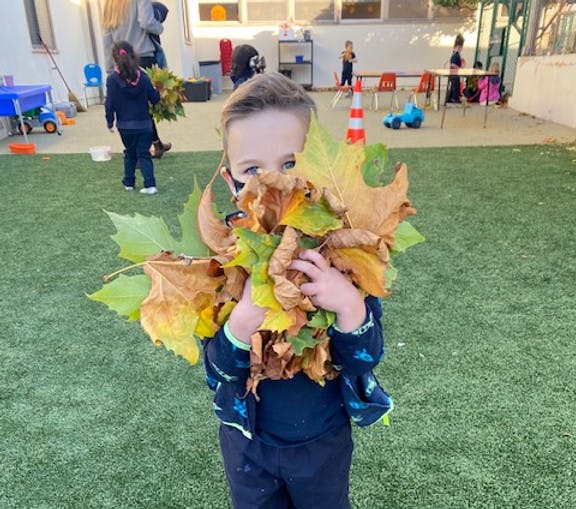 Child peeking over a large armful of colorful autumn leaves