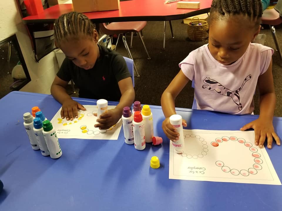 Two children using dot markers on paper at a table
