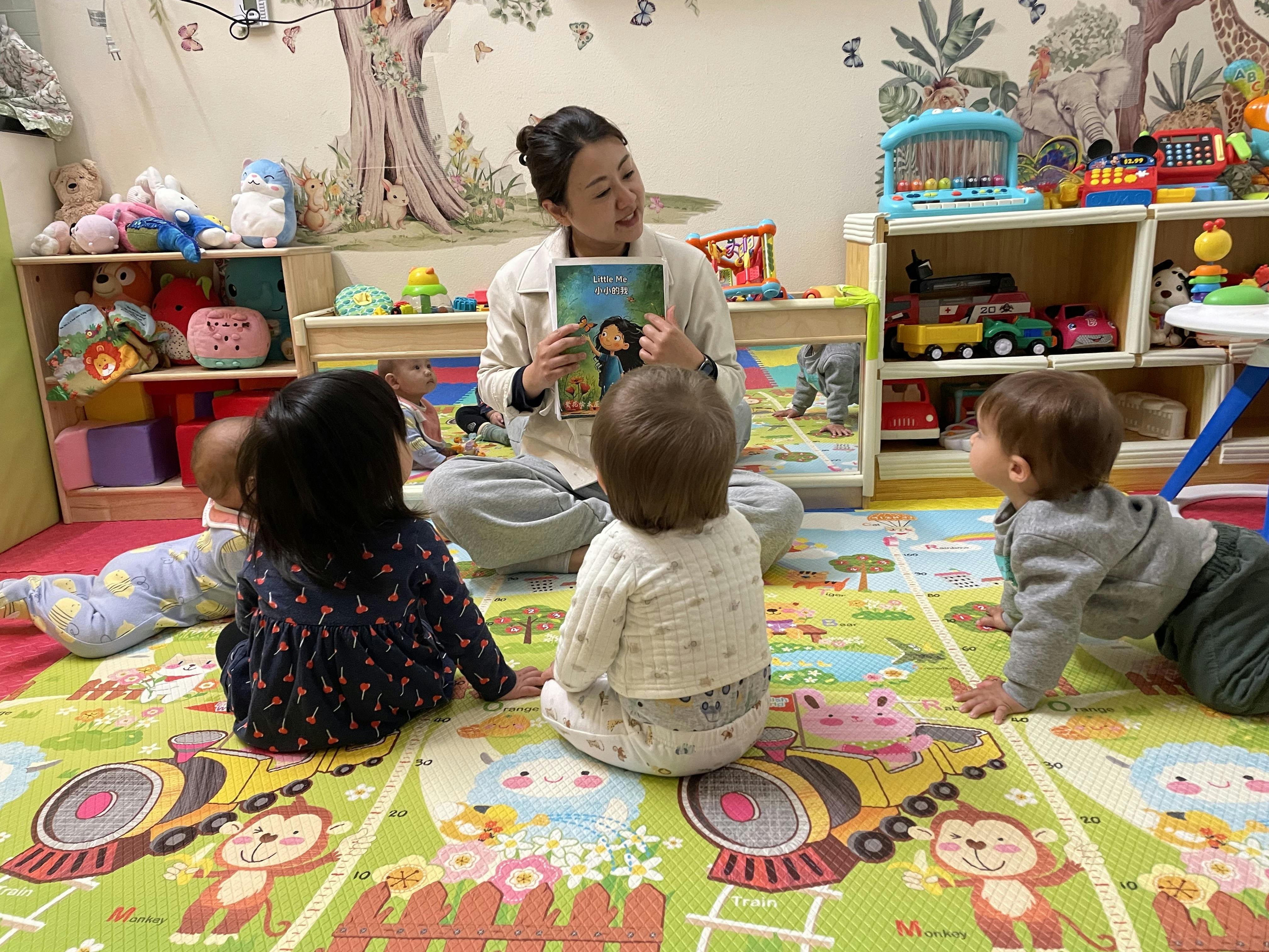 Adult sitting on a play mat reading a book to several children