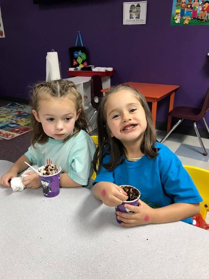 Two children sitting at a table with cups of dessert