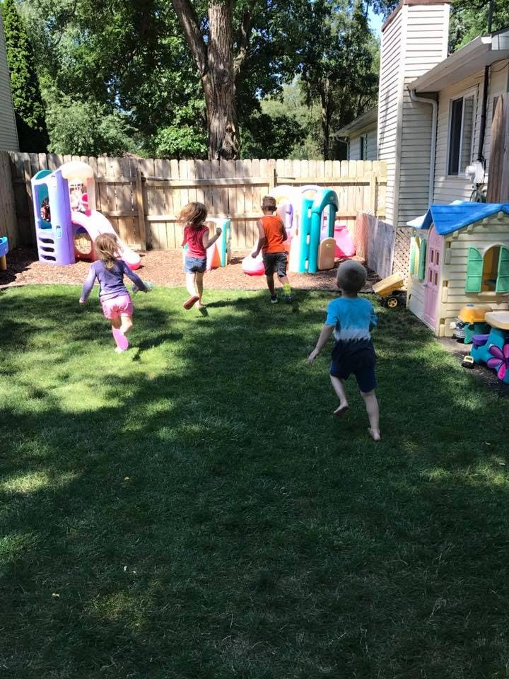 Children playing in a backyard with playhouses and climbing structures