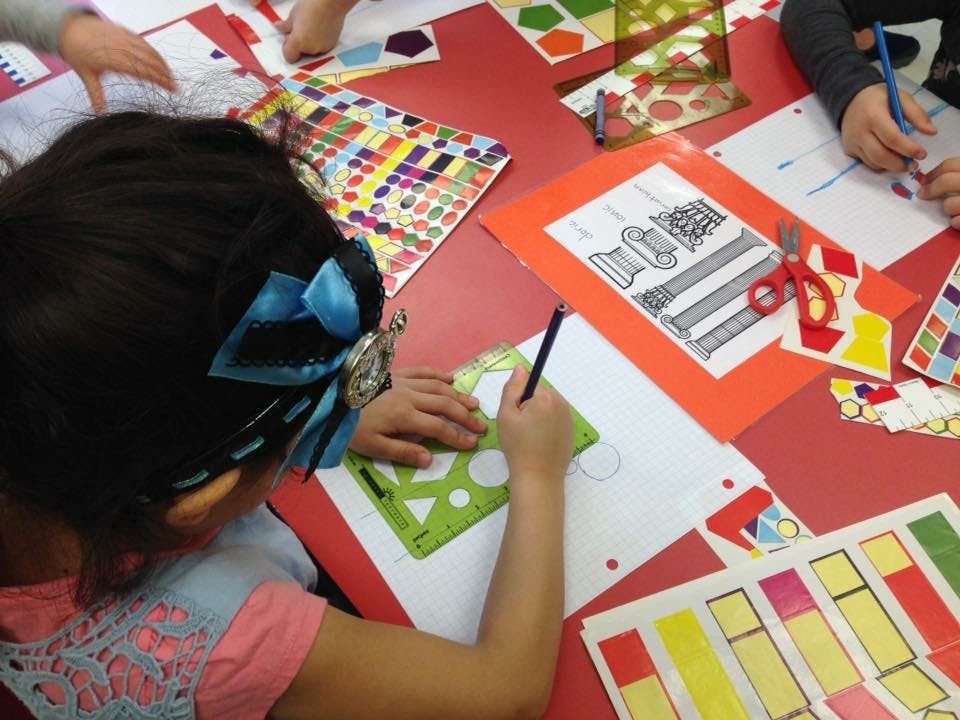 Child drawing with a stencil at a table with other children