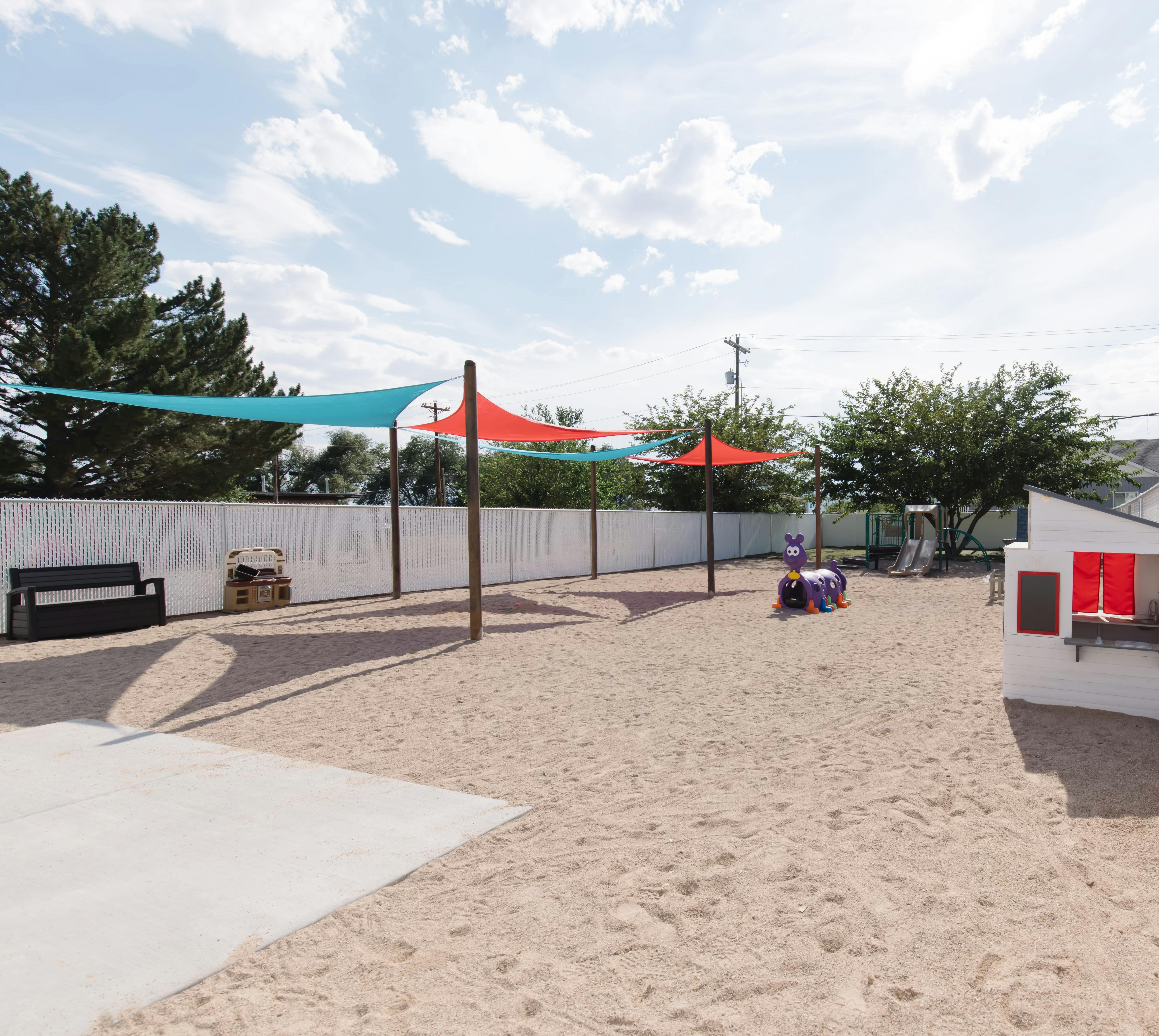 Outdoor play area with sand, shade sails, and play structures