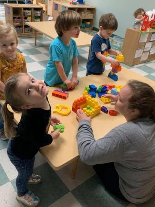 Adult and children playing with building blocks at a table in a classroom