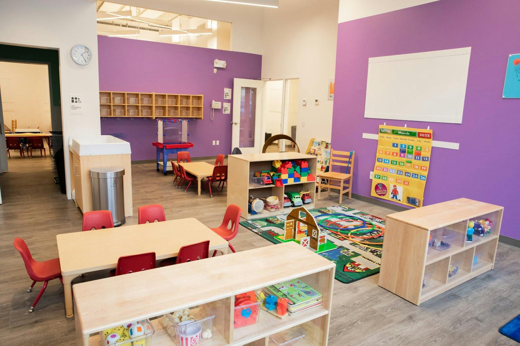 Classroom with child-sized tables and chairs, shelves with toys, and a March 2022 calendar