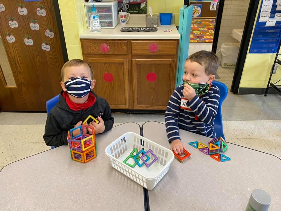 Two children wearing masks playing with magnetic blocks at a table