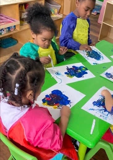Three children painting at a green table