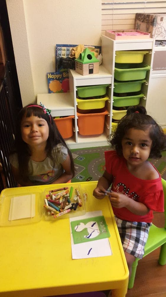 Two children sitting at a yellow table with crayons and paper