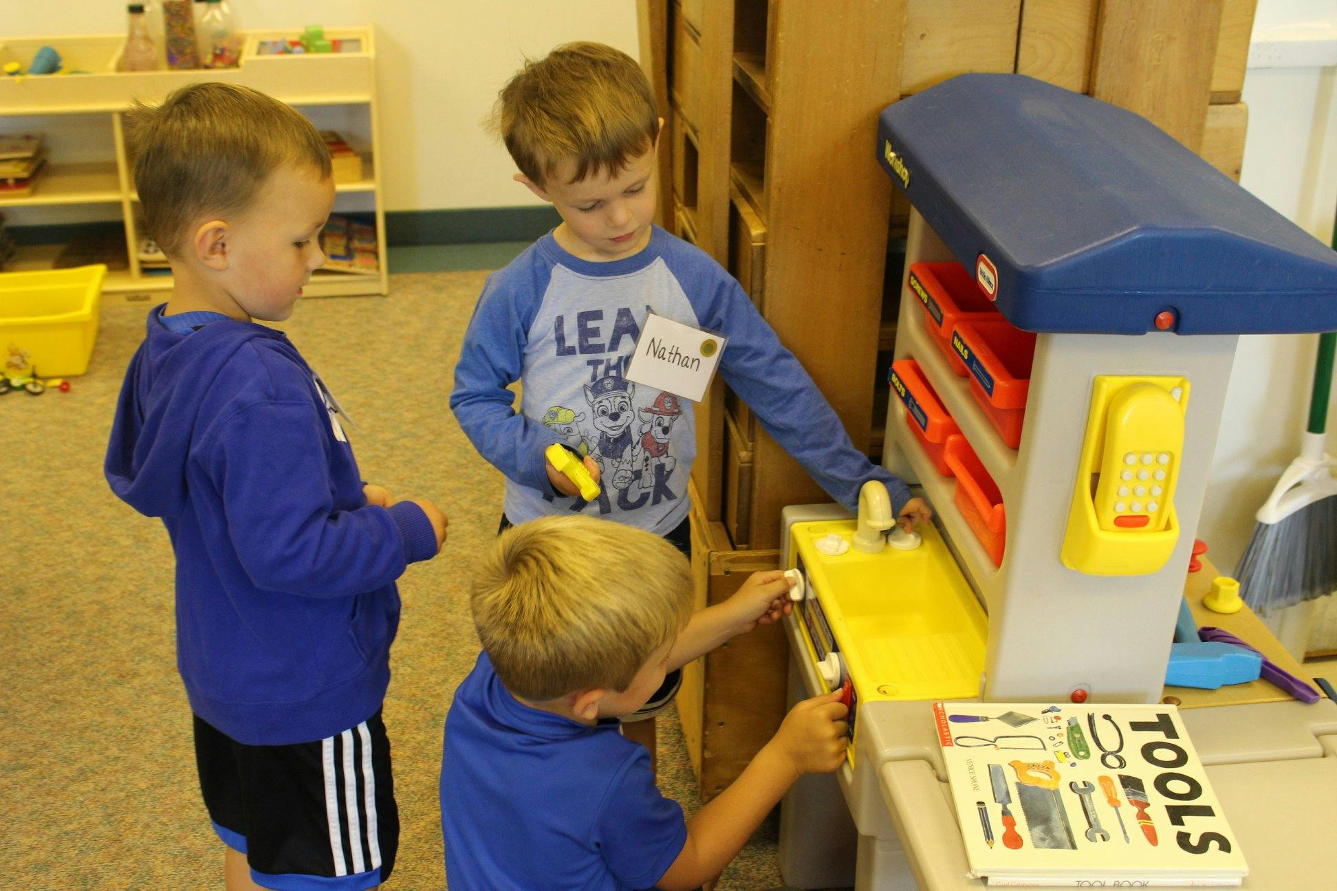 Three children playing with a toy workbench