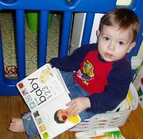 Child sitting in a basket holding an open book