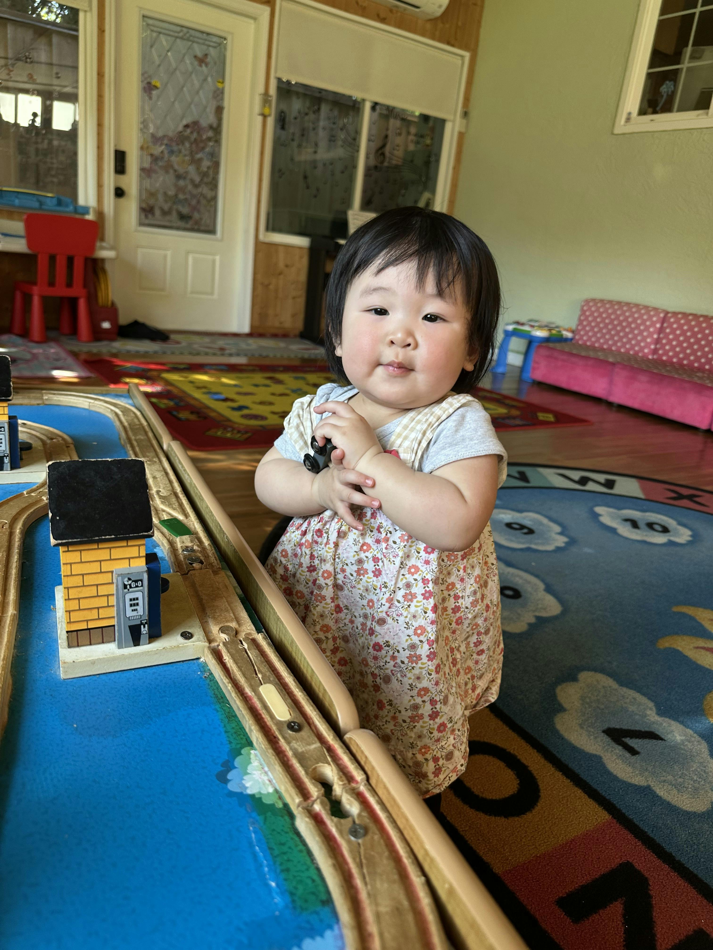 Child sitting on a rug next to a toy train track