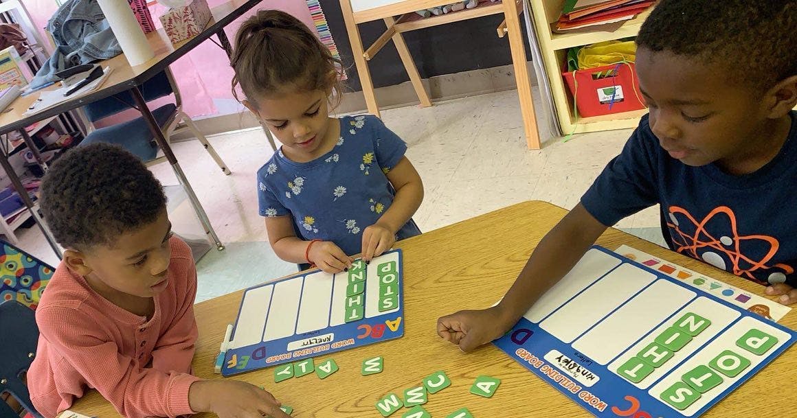 Three children playing with letter tiles and learning boards at a table