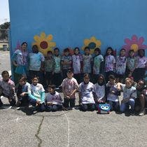 Group of children and adults posing in front of a blue wall with flower murals